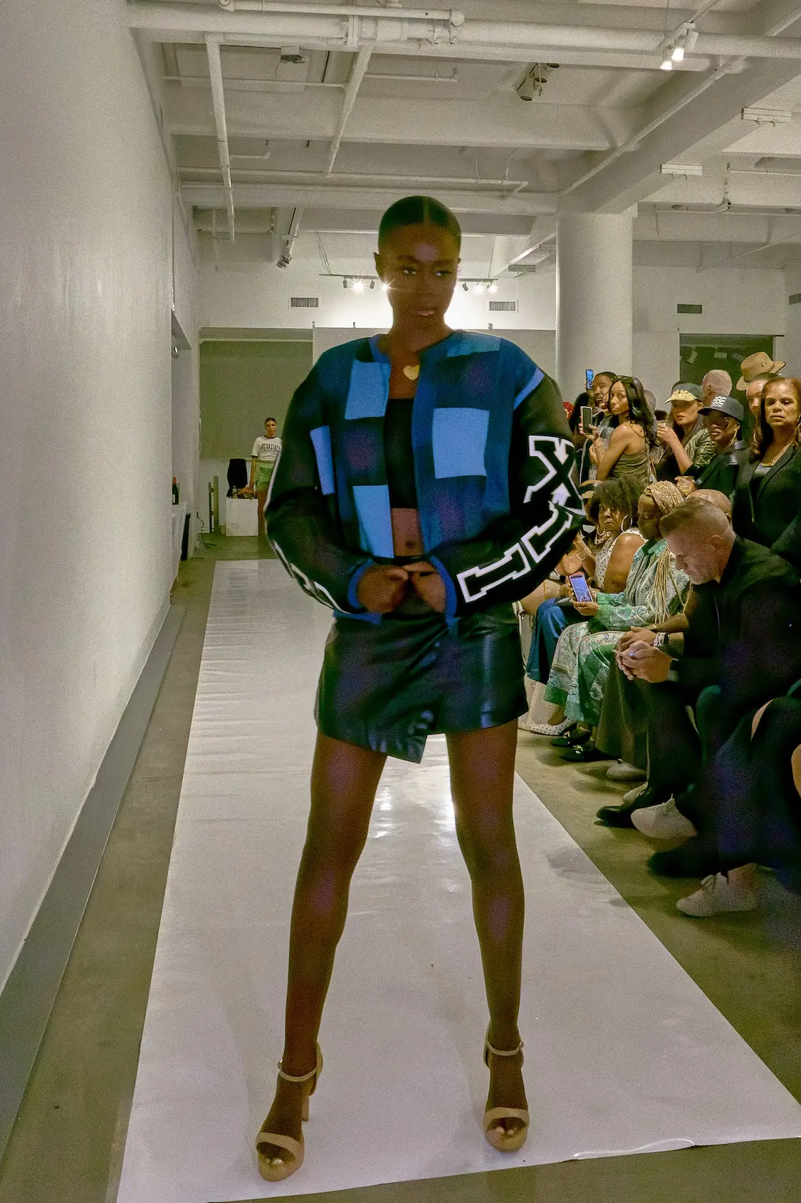 A model wears a blue and black patchwork jacket with oversized graphic sleeves and a dark mini skirt during BICOASTAL COLLECTION’s SS27 presentation.
