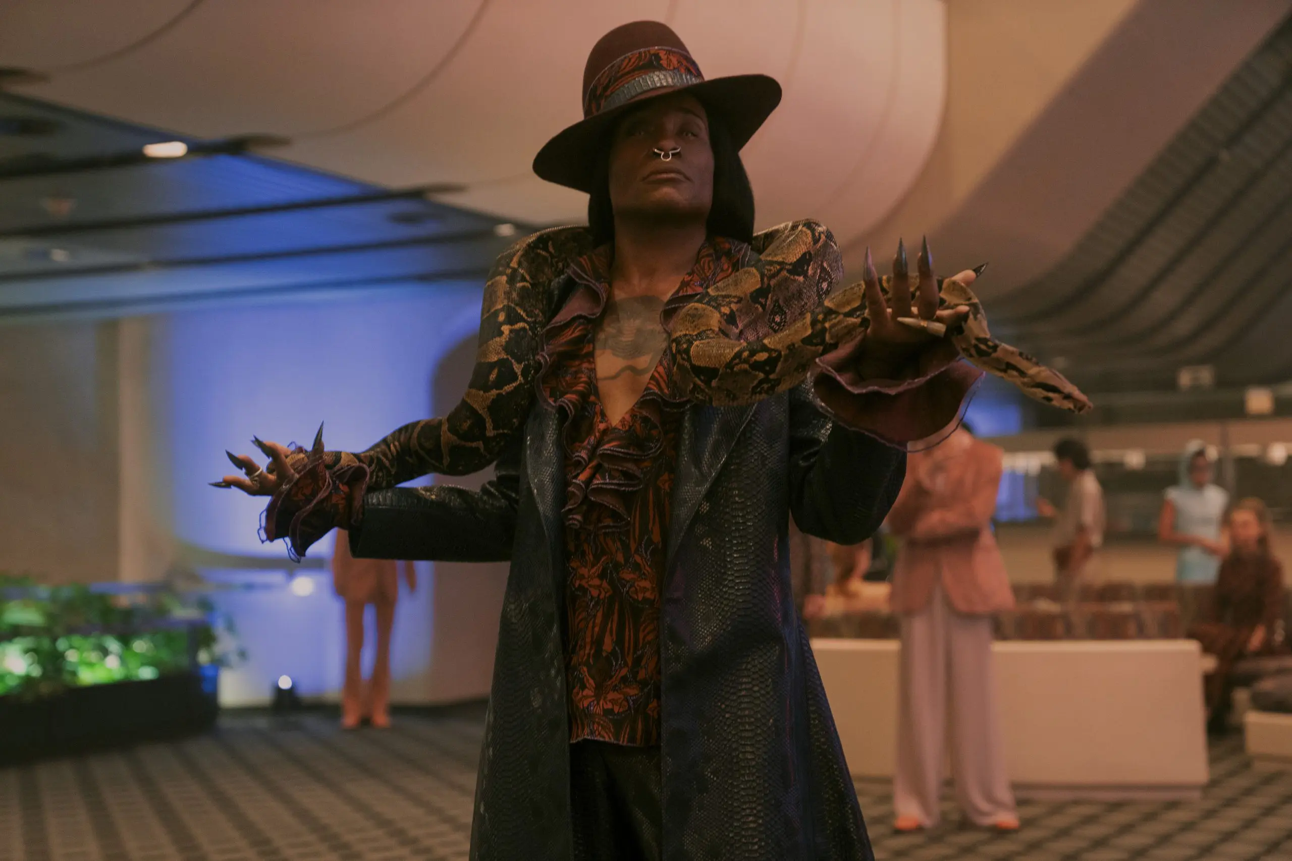 Billy Porter as Magno Stift in a snakeskin-patterned outfit, wide-brimmed hat and dramatic pointed nails in The Hunger Games: Sunrise on the Reaping.