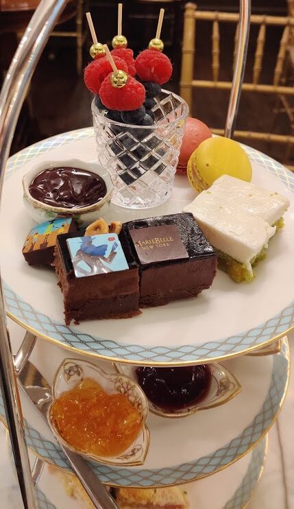 A tiered serving tray with fruit, chocolates, scones, and sandwiches