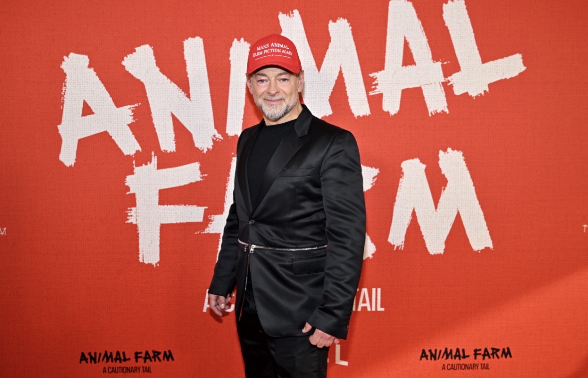 Andy Serkis poses in front of a red backdrop with text that reads "Animal Farm."