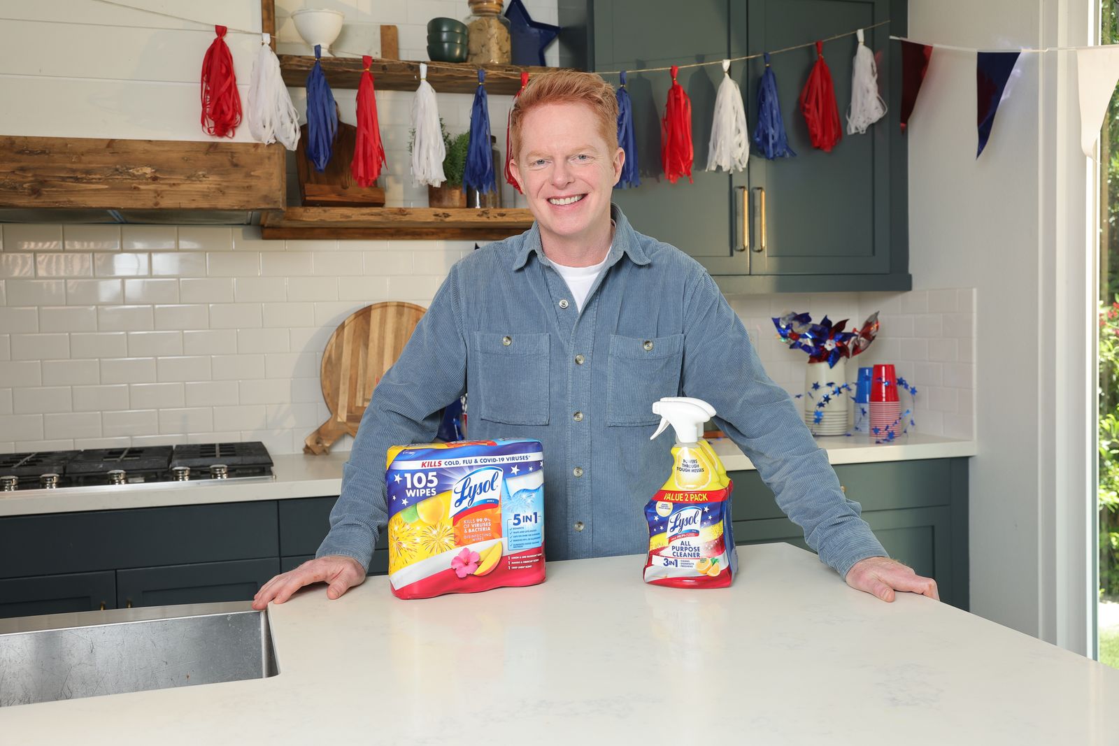 Actor Jesse Tyler Ferguson smiling and holding limited-edition Lysol products while posing in a bright, modern kitchen.